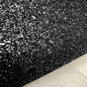 May include: Black glitter fabric with a fine, sparkly texture. The glitter is densely packed and creates a shimmering effect.