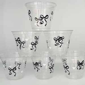 May include: Six clear plastic cups with black bows and white hearts printed on them.
