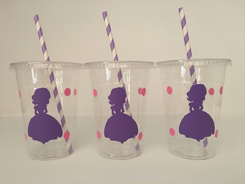 May include: Three clear plastic cups with purple and pink designs. Each cup has a purple silhouette of a princess with a crown and a pink polka dot pattern. Each cup has a purple and white striped straw.