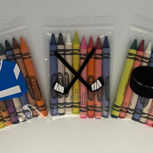 May include: Three clear plastic bags filled with Crayola crayons. The bags are decorated with hockey-themed cutouts. One bag has a blue hockey jersey, one has a pair of crossed hockey sticks, and one has a black hockey puck.