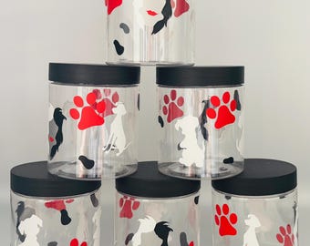May include: A stack of clear plastic jars with black lids. The jars are decorated with red paw prints, white dog silhouettes, and black and gray abstract shapes. The jars are arranged in a pyramid shape.