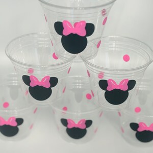 Puede incluir: Seis vasos de pl&aacute;stico transparentes con lunares rosas y un dise&ntilde;o de Minnie Mouse negro y rosa.