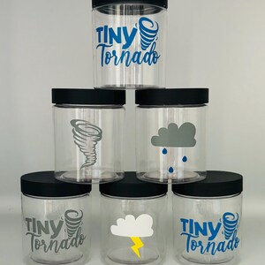 May include: Six clear glass jars with black lids. The jars have different weather-themed designs, including a tornado, a cloud with rain, a cloud with lightning, and the text "Tiny Tornado".