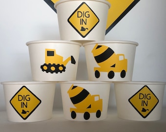 May include: Six white paper cups with construction vehicle designs.  The cups have yellow and black designs of a cement mixer truck, a bulldozer, and a yellow diamond sign with the text "DIG IN".