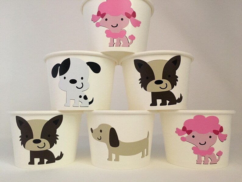 Pu&ograve; includere: Set di sei bicchieri di carta bianchi con diversi disegni di animali. I bicchieri presentano un cane macchiato bianco e nero, un cane marrone, un cane marrone e bianco, un bassotto marrone, un barboncino rosa e un barboncino rosa con un fiocco.