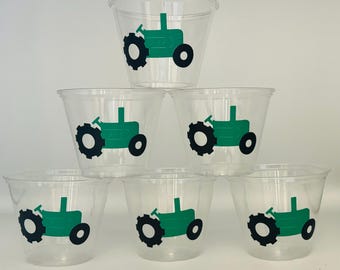 May include: Six clear plastic cups with green tractor designs. The tractors are green with black wheels and a black exhaust pipe.