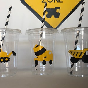 May include: Three clear plastic cups with black and white striped straws. Each cup has a different construction vehicle sticker: a yellow bulldozer, a yellow cement mixer, and a yellow dump truck.