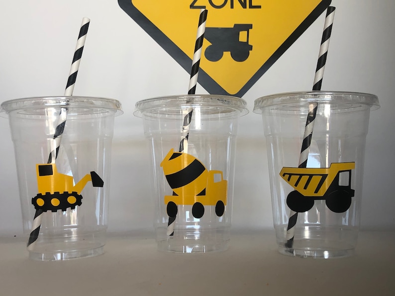 May include: Three clear plastic cups with black and white striped straws. Each cup has a different construction vehicle sticker: a yellow bulldozer, a yellow cement mixer, and a yellow dump truck.