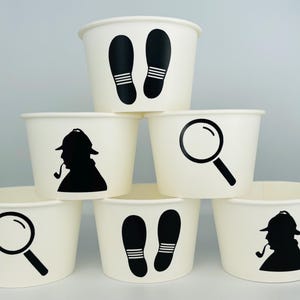 Puede incluir: Seis vasos de papel blancos con siluetas negras de una lupa, huellas y un detective con una pipa. Los vasos est&aacute;n apilados en forma de pir&aacute;mide.