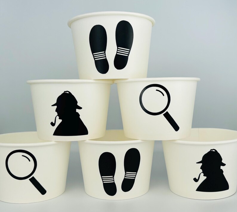 Puede incluir: Seis vasos de papel blancos con siluetas negras de una lupa, huellas y un detective con una pipa. Los vasos est&aacute;n apilados en forma de pir&aacute;mide.