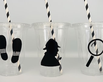 May include: Three clear plastic cups with black and white striped straws. Each cup has a different black silhouette design: footprints, a detective with a hat and pipe, and a magnifying glass.