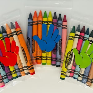 May include: Three bags of Crayola crayons, each with a different colored handprint sticker. The bags are filled with a variety of colors, including red, blue, green, yellow, orange, and purple.