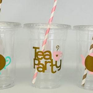 Puede incluir: Tres vasos de pl&aacute;stico transparente con tapas y pajitas. Cada vaso tiene un dise&ntilde;o diferente: una tetera, las palabras "Tea Party" con una taza de t&eacute; y otra tetera. Las pajitas son rayadas.