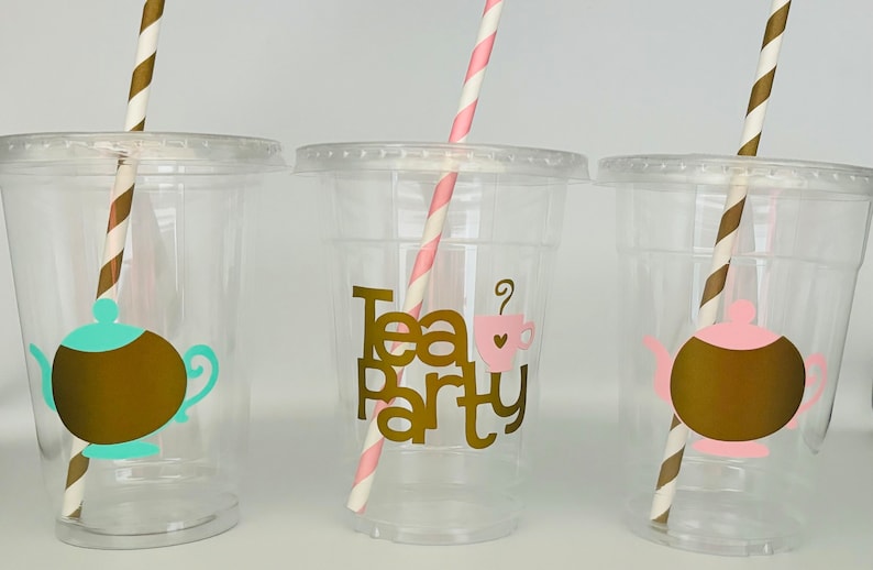 Puede incluir: Tres vasos de pl&aacute;stico transparente con tapas y pajitas. Cada vaso tiene un dise&ntilde;o diferente: una tetera, las palabras "Tea Party" con una taza de t&eacute; y otra tetera. Las pajitas son rayadas.