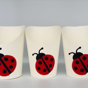 May include: Three white paper cups with a red and black ladybug design. The ladybugs have black spots and are facing to the right.