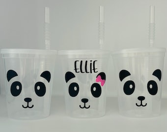 May include: Three clear plastic cups with black panda faces and straws. One cup has the name "Ellie" written on it.