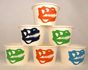 May include: Six white paper cups with dinosaur skull designs. The cups feature different colored dinosaur skulls: orange, green, blue, and black.