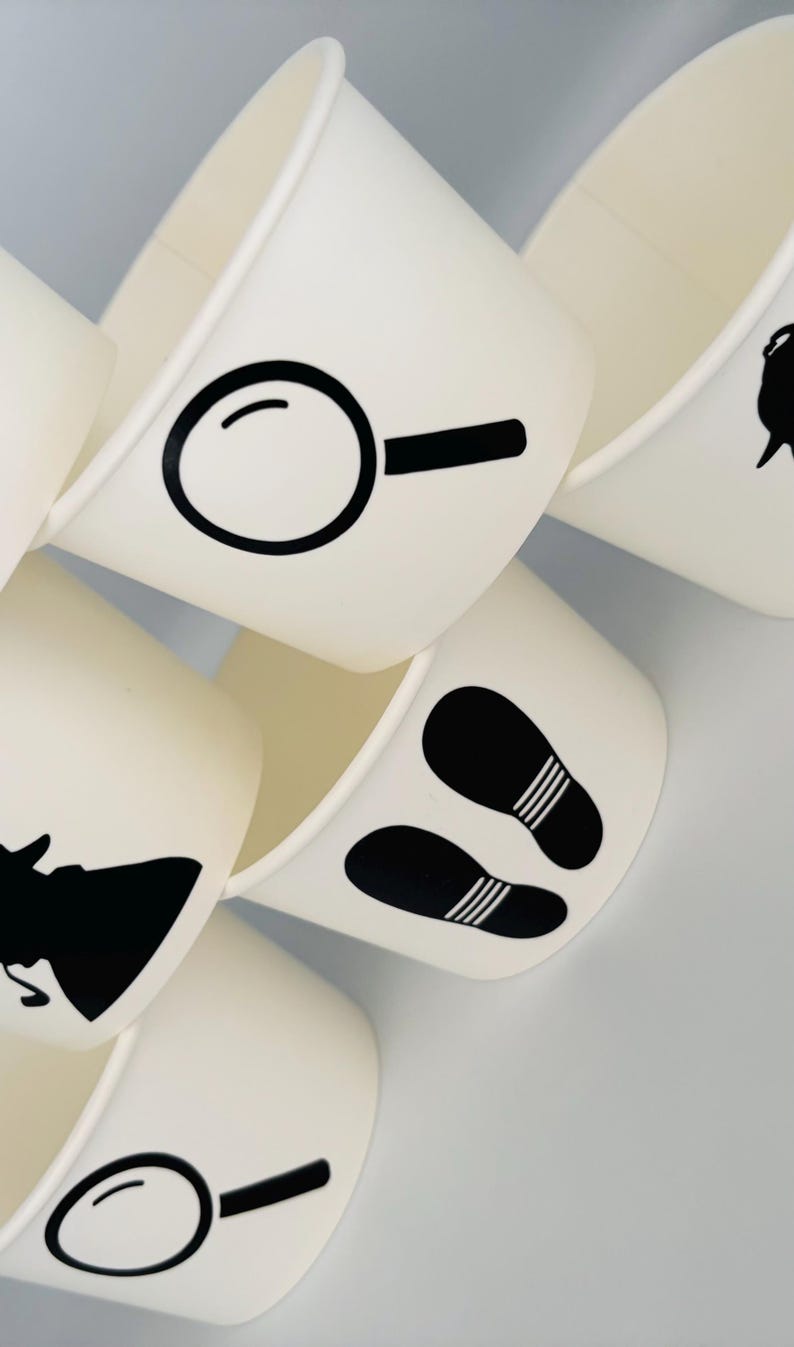 Puede incluir: Conjunto de seis vasos de papel blanco con dise&ntilde;os de silueta negra. Los dise&ntilde;os incluyen una lupa, huellas y una silueta de una persona con sombrero.