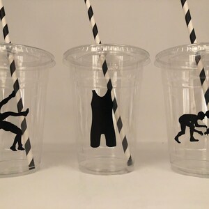 K&ouml;nnte beinhalten: Drei durchsichtige Plastikbecher mit schwarz-wei&szlig; gestreiften Strohhalmen. Jeder Becher hat eine schwarze Silhouette eines Wrestlers darauf. Die Silhouetten zeigen einen Ringer in einem Ringer-Tanktop, einen Ringer in einer Takedown-Position und zwei Ringer im Clinch.