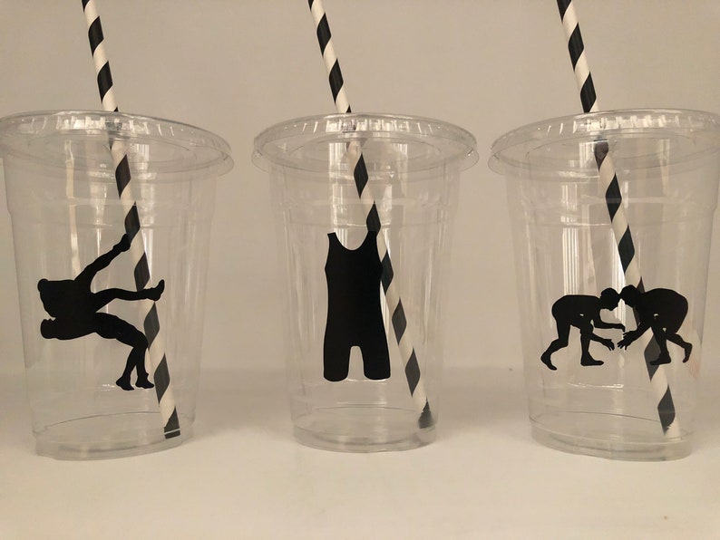K&ouml;nnte beinhalten: Drei durchsichtige Plastikbecher mit schwarz-wei&szlig; gestreiften Strohhalmen. Jeder Becher hat eine schwarze Silhouette eines Wrestlers darauf. Die Silhouetten zeigen einen Ringer in einem Ringer-Tanktop, einen Ringer in einer Takedown-Position und zwei Ringer im Clinch.