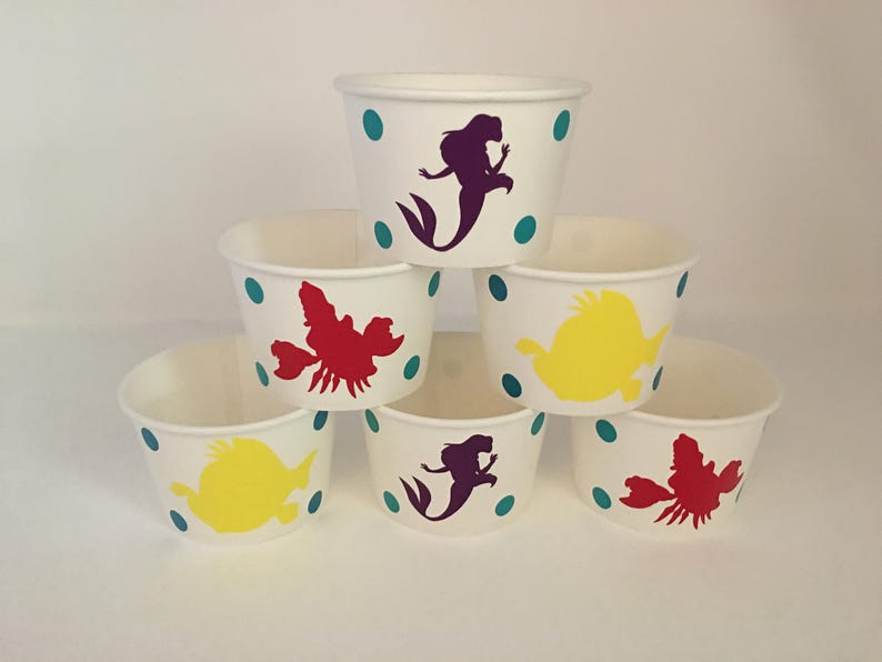May include: Six white paper cups with teal polka dots and various colourful cartoon characters, including a mermaid, a crab, and a fish.