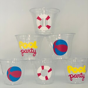 May include: Six clear plastic cups with different pool party designs. The designs include a yellow "Pool Party" text, a red and white life preserver, and a red and blue beach ball.
