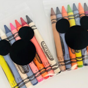 May include: Two clear plastic bags filled with Crayola crayons in various colors. Each bag is decorated with a black Mickey Mouse head. The crayons are labeled with their respective colors, such as "red", "orange", and "blue".