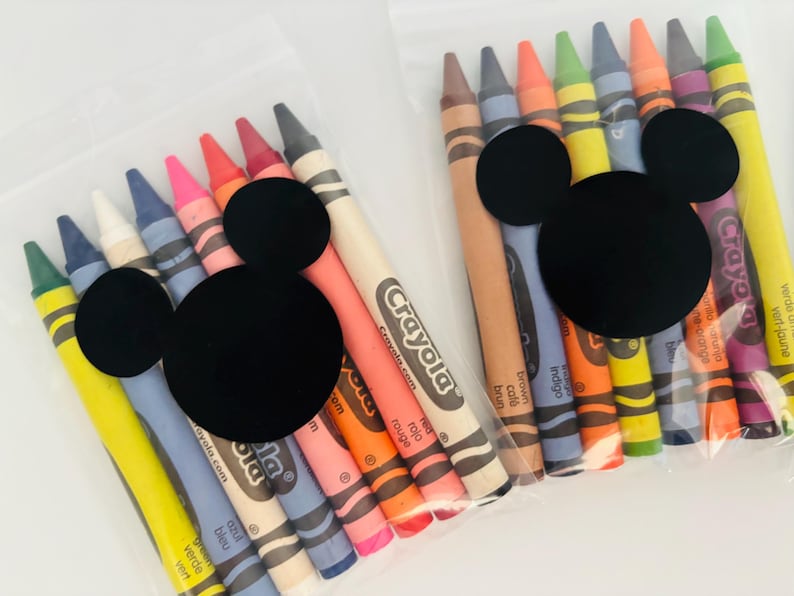 May include: Two clear plastic bags filled with Crayola crayons in various colors. Each bag is decorated with a black Mickey Mouse head. The crayons are labeled with their respective colors, such as "red", "orange", and "blue".