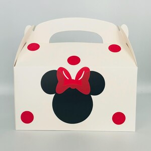 Puede incluir: Caja de regalo blanca con un dise&ntilde;o de Minnie Mouse rojo y negro. La caja tiene un asa y lunares rojos.