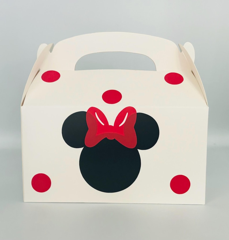 Puede incluir: Caja de regalo blanca con un dise&ntilde;o de Minnie Mouse rojo y negro. La caja tiene un asa y lunares rojos.