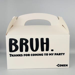 May include: White cardboard party favor box with a black handle. The box has the word "BRUH." printed in black, followed by "THANKS FOR COMING TO MY PARTY" and " -COHEN".