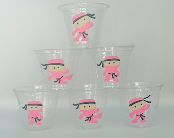 May include: Six clear plastic cups with pink ninja characters on them. The ninjas are wearing black belts and have black eyes.