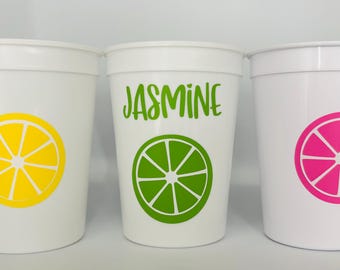 May include: Three white plastic cups with different citrus fruit designs. The cup in the middle has the name "JASMINE" written on it.