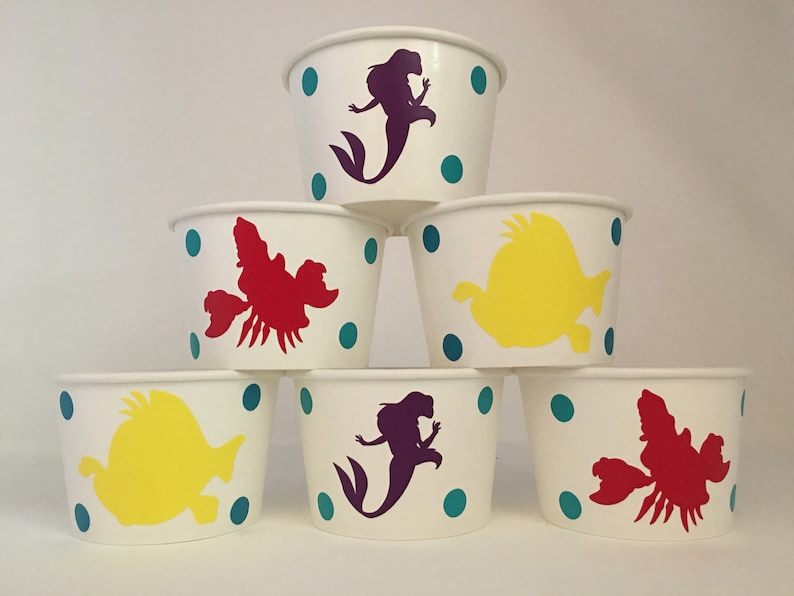 May include: Six white paper cups with teal polka dots and various Disney characters. The characters include Ariel the mermaid, Sebastian the crab, and Flounder the fish.