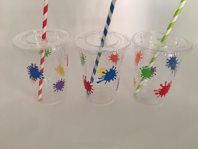 May include: Three clear plastic cups with colorful paint splatter designs and matching striped straws. The cups are perfect for a party or celebration.