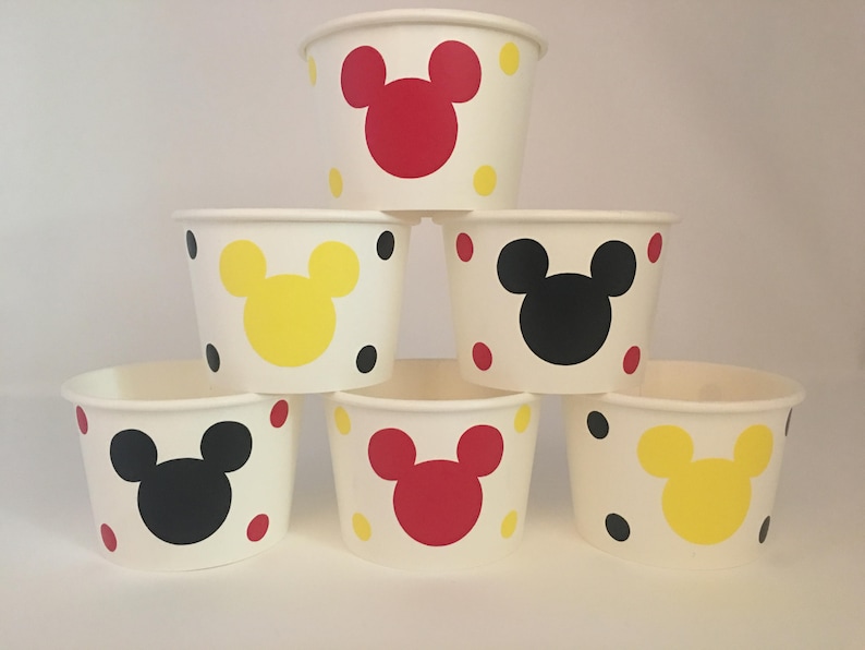K&ouml;nnte beinhalten: Sechs wei&szlig;e Pappbecher mit Mickey-Maus-Motiven. Jeder Becher hat einen Mickey-Maus-Kopf in einer anderen Farbe: rot, gelb, schwarz, rot, gelb und schwarz. Die Becher sind pyramidenf&ouml;rmig gestapelt.