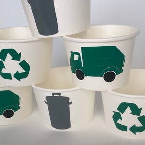 May include: Set of six white paper cups with green and gray recycling themed designs. The designs include a recycling symbol, a garbage truck, and a trash can.