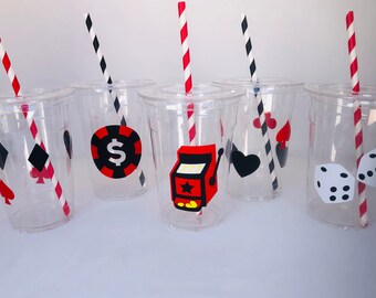 May include: Six clear plastic cups with red and black striped straws. Each cup has a different casino-themed design: a dollar sign, a slot machine, a heart, a spade, a diamond, and dice.