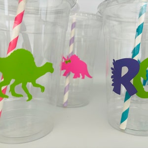 May include: Clear plastic cups with dinosaur silhouettes in green and pink. Each cup has a colorful paper straw. One cup has the word "ROAR" in purple and green. Party supplies.