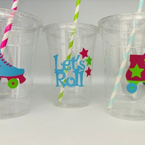 May include: Three clear plastic cups with straws and colorful roller skate designs. The middle cup has the text "Let's Roll" in blue letters with green and red stars.