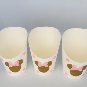 K&ouml;nnte beinhalten: Drei wei&szlig;e Pappbecher mit rosa Punkten und einem goldenen Minnie Mouse Kopf mit einer rosa Schleife auf jedem Becher.