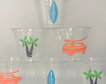 May include: Six clear plastic cups with different designs. The designs include a surfboard, a palm tree, and a vintage van. The cups are stacked in a pyramid shape.