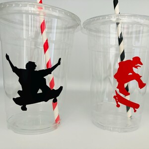 Puede incluir: Dos vasos de pl&aacute;stico transparentes con pajitas rayadas rojas y negras. Un vaso tiene una silueta negra de una persona haciendo skate, el otro tiene una silueta roja de una persona haciendo skate.