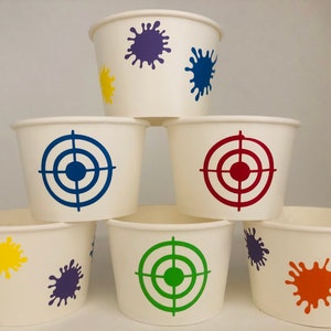 Peut inclure: Six gobelets en papier blanc avec des motifs diff&eacute;rents. Trois gobelets ont une cible en forme de bullseye bleue, rouge et verte. Trois gobelets ont des &eacute;claboussures de peinture violette, bleue, jaune et orange.