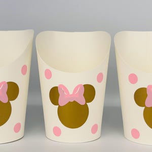 May include: Three white paper cups with pink polka dots and a gold Minnie Mouse head with a pink bow on each cup.