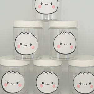 May include: Six clear glass jars with white lids and cute cartoon dumpling faces with pink cheeks. The jars are stacked in a pyramid shape.