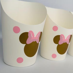 K&ouml;nnte beinhalten: Wei&szlig;e Pappbecher mit einem goldenen und rosafarbenen Minnie Mouse-Design. Die Becher haben rosa Punkte und sind perfekt f&uuml;r eine Party.