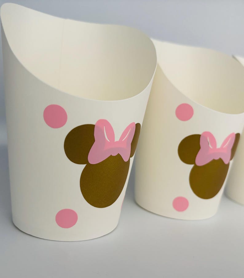 K&ouml;nnte beinhalten: Wei&szlig;e Pappbecher mit einem goldenen und rosafarbenen Minnie Mouse-Design. Die Becher haben rosa Punkte und sind perfekt f&uuml;r eine Party.