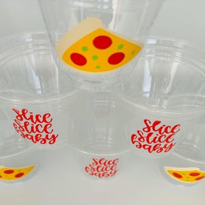 Op de afbeelding: Set van zes doorzichtige plastic bekers met rode en gele pizza-plakjes ontwerpen en de tekst "Slice Slice Baby" op elke beker.