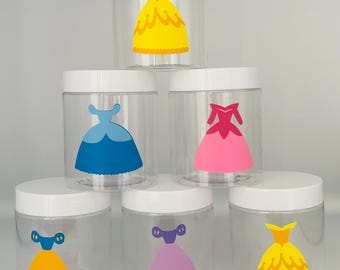 May include: Six clear plastic jars with white lids, each decorated with a colorful dress design. The dresses are in shades of yellow, blue, pink, and purple. The jars are arranged in a stacked formation.